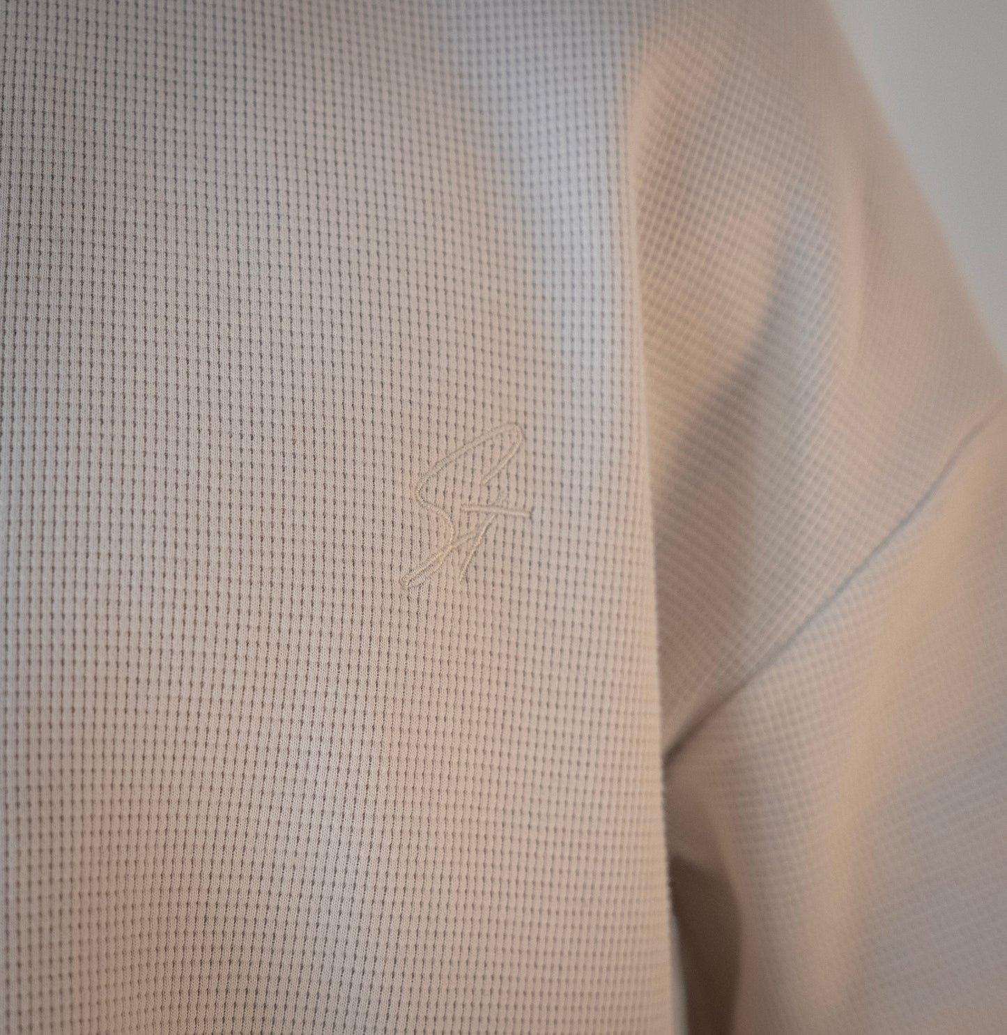 Close-up of embroidered Stingem logo on left chest of white cotton jumper.