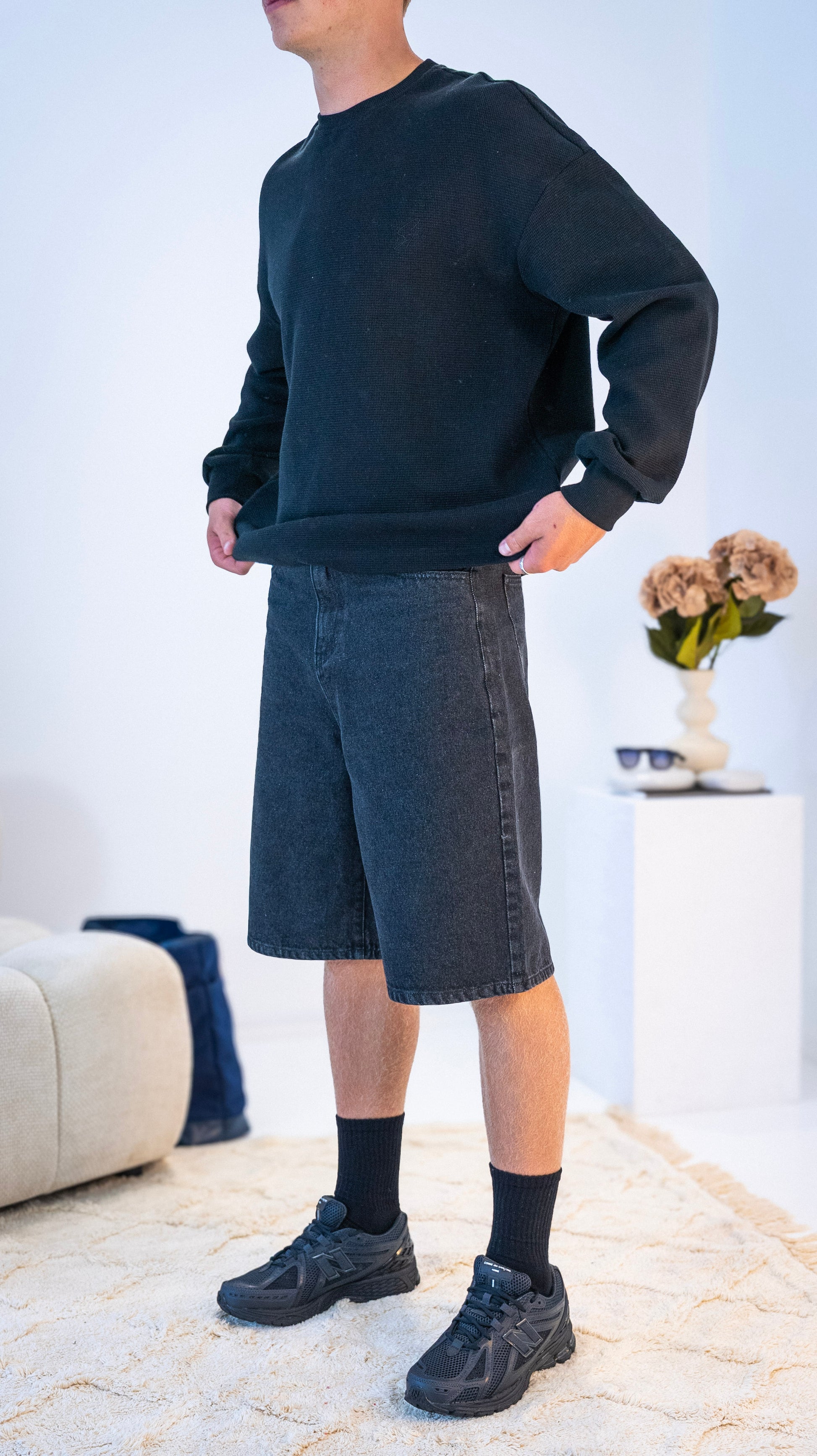 Side view of model wearing black Stingem cotton shorts with black crew jumper.
