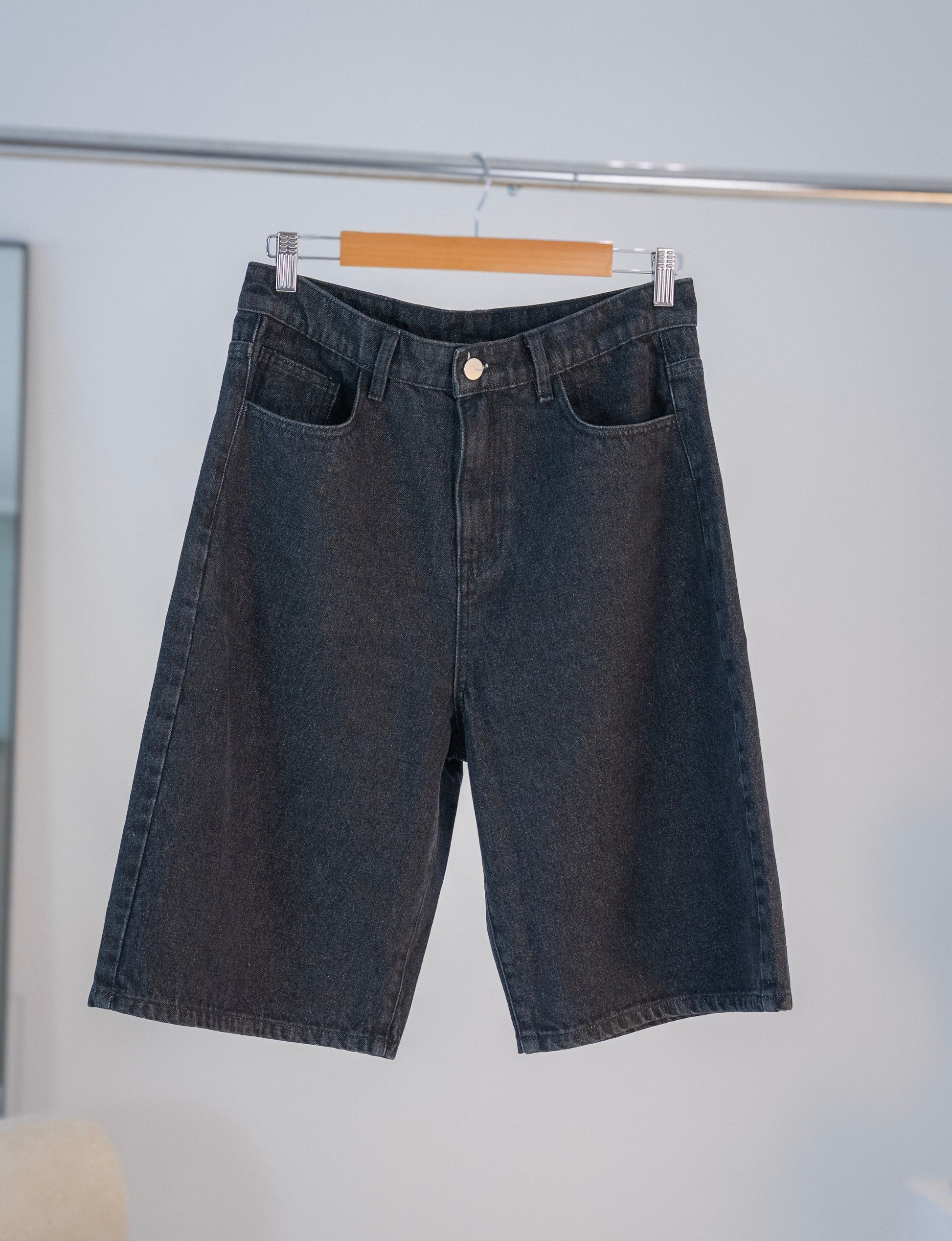 Front view of black Stingem cotton shorts hanging on wooden hanger.