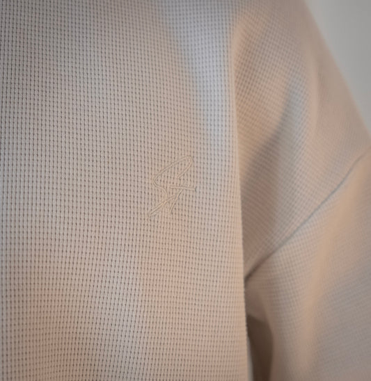 Close-up of embroidered Stingem logo on left chest of white cotton jumper.
