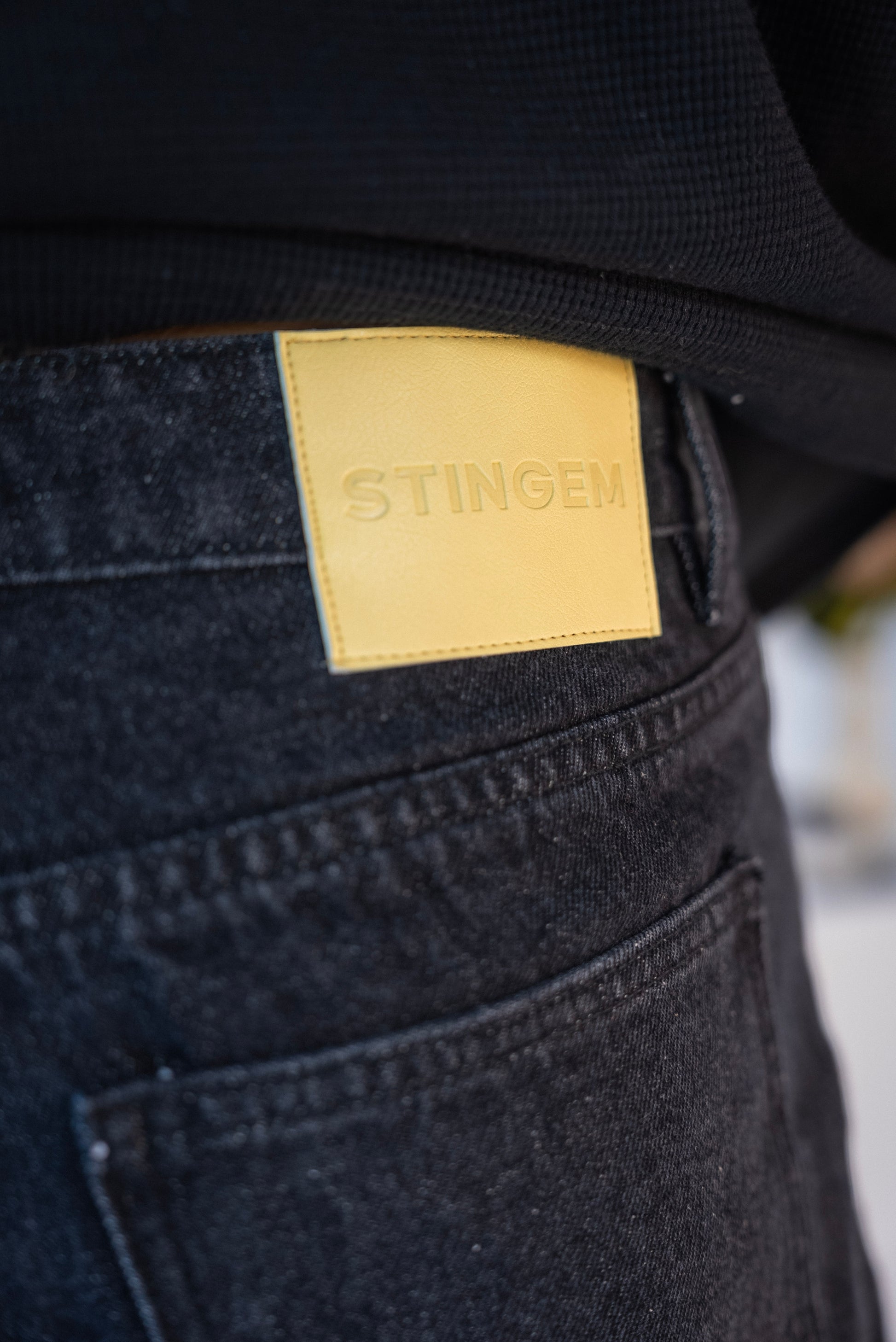 Close-up of Stingem leather logo patch on back waistband of black cotton shorts.