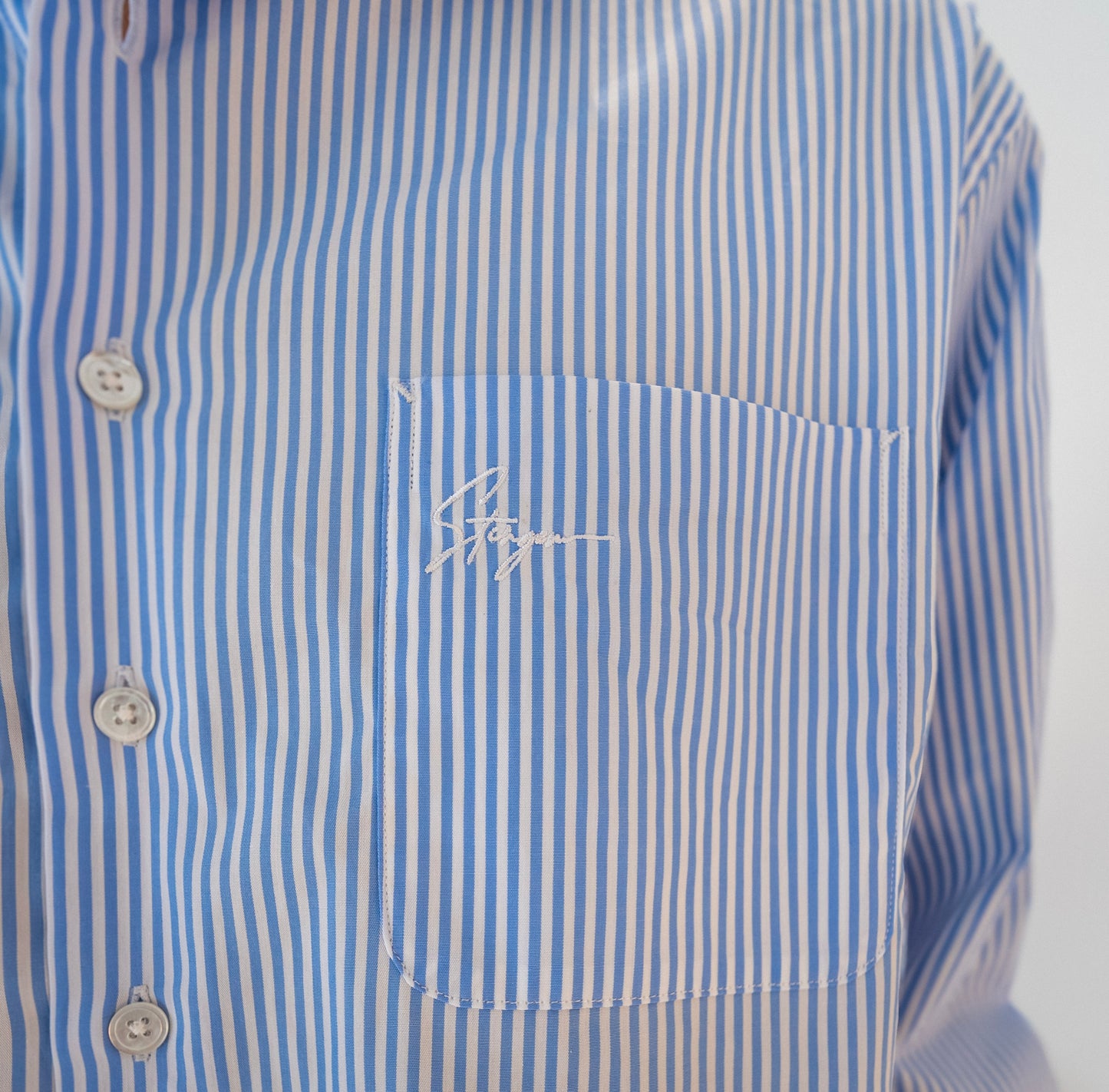 Close-up of Stingem white and blue striped cotton shirt chest pocket with embroidered logo.