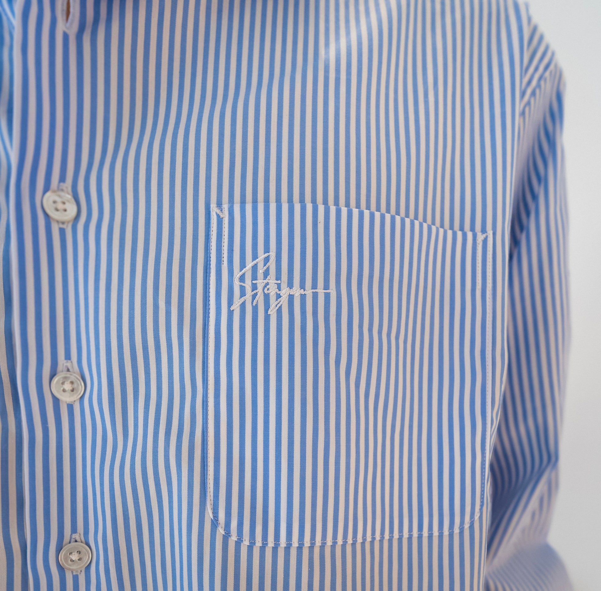 Close-up of Stingem white and blue striped cotton shirt chest pocket with embroidered logo.