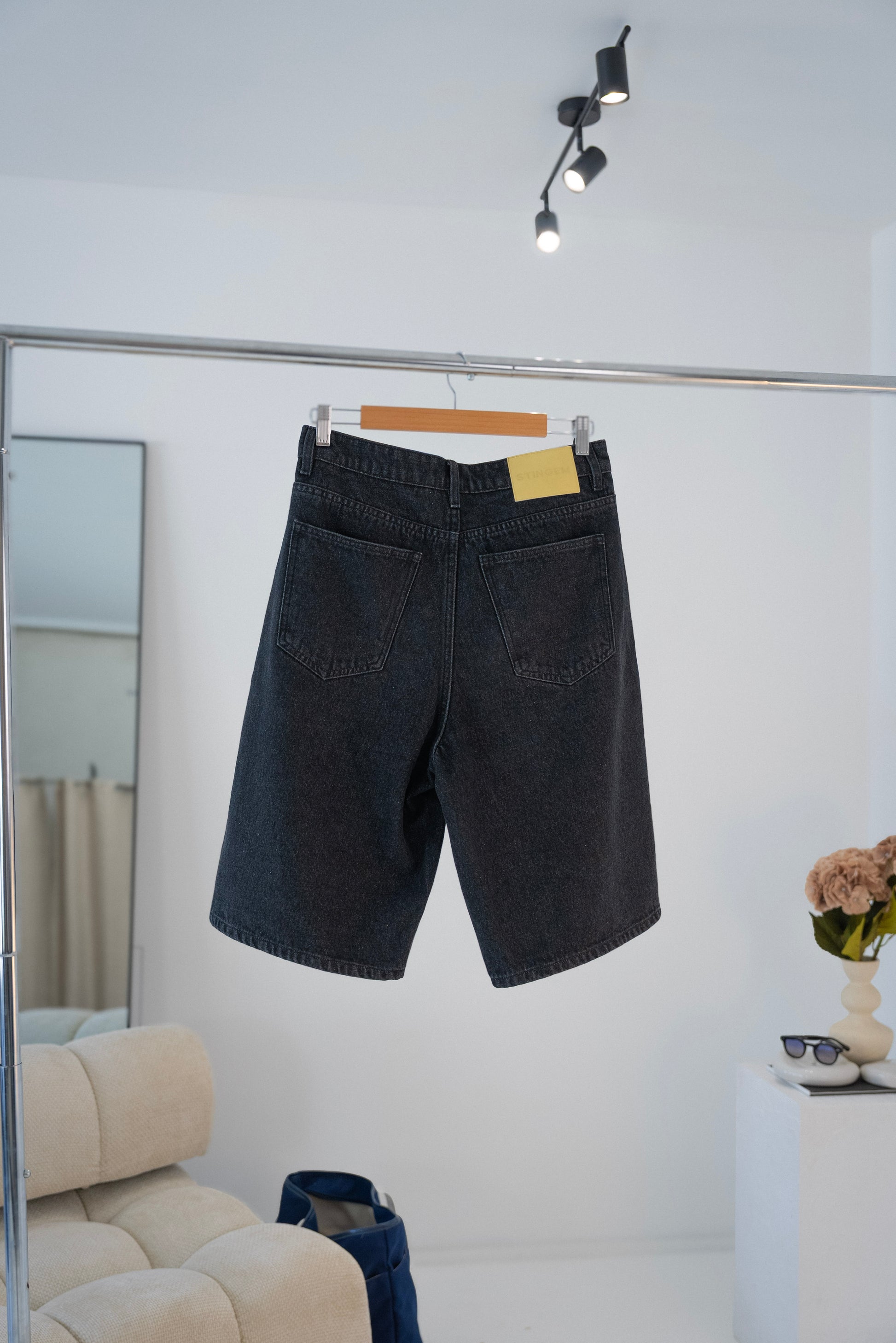 Back view of black Stingem cotton shorts hanging on clothing rack.