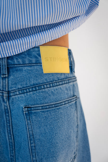 Close-up of Stingem leather logo patch on back waistband of blue washed jeans.