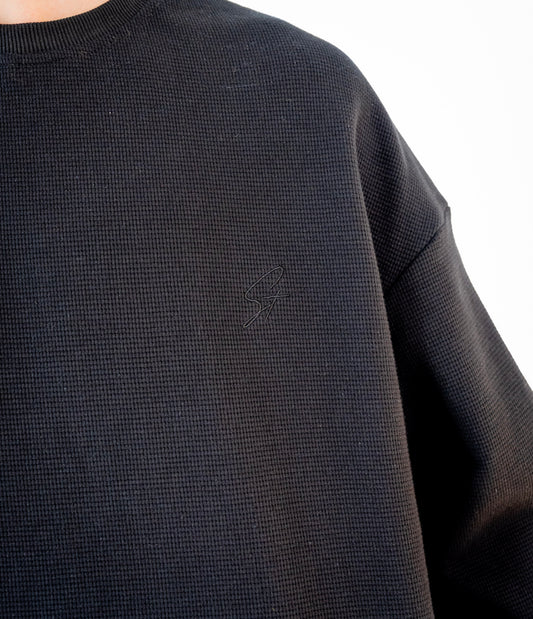 Close-up of embroidered Stingem logo on left chest of black cotton jumper.